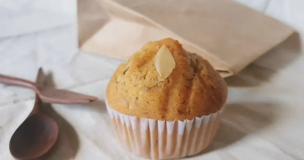 Freshly baked banana muffins arranged on a wooden tray, golden-brown and fluffy, with a broken muffin showing its moist texture. Surrounded by ripe bananas, a bowl of flour, and walnuts, highlighting the homemade feel. Text overlay reads: 'Simple Banana Muffin Recipe: Ready in Just 30 Minutes.' Blog domain www.bananarecipess.com is displayed in the footer.